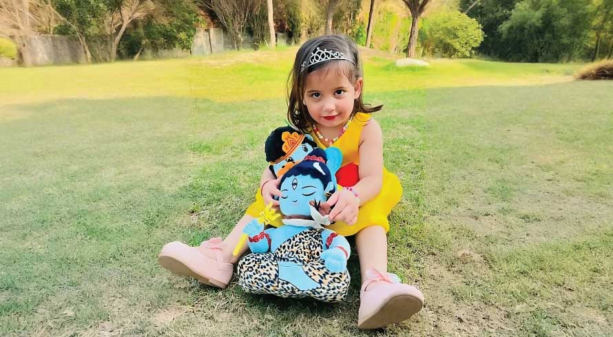 Girl Child holding mantra chanting shiva and krishna plush toys outdoors on grass