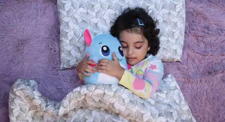 Child holding a luna plush pillow toy and sleeping on bed