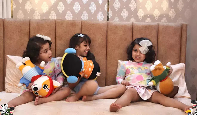 Three children sitting on a bed with colorful plush dog, penguin and tiger toys, smiling and posing