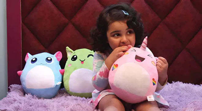 Child holding a pink plush toy with two other colorful plush toys on a purple surface.
