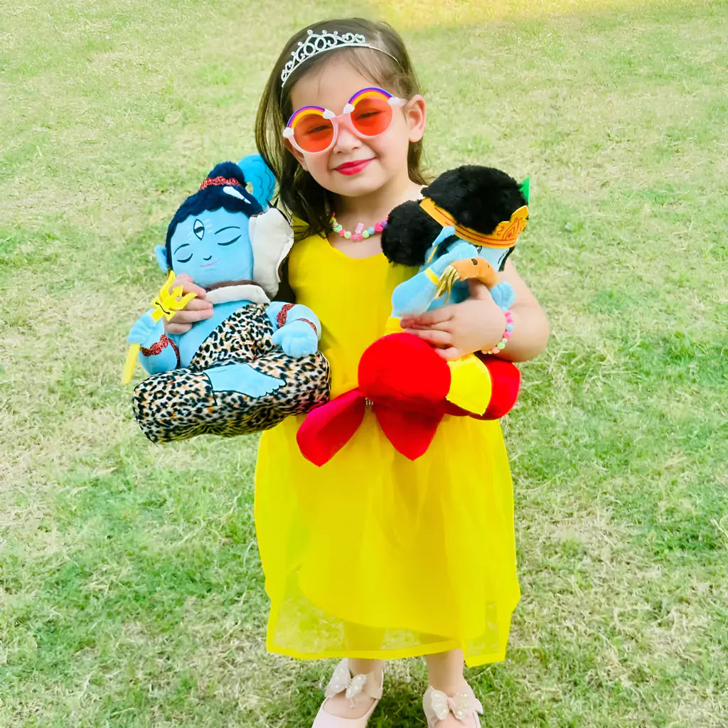 a little girl smiling and holding aurbo mantra chanting shiva and krishna plush toys